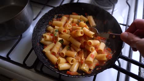 cocinar pasta rigatoni con crema de tomate en una sartén, mezclar con una cuchara