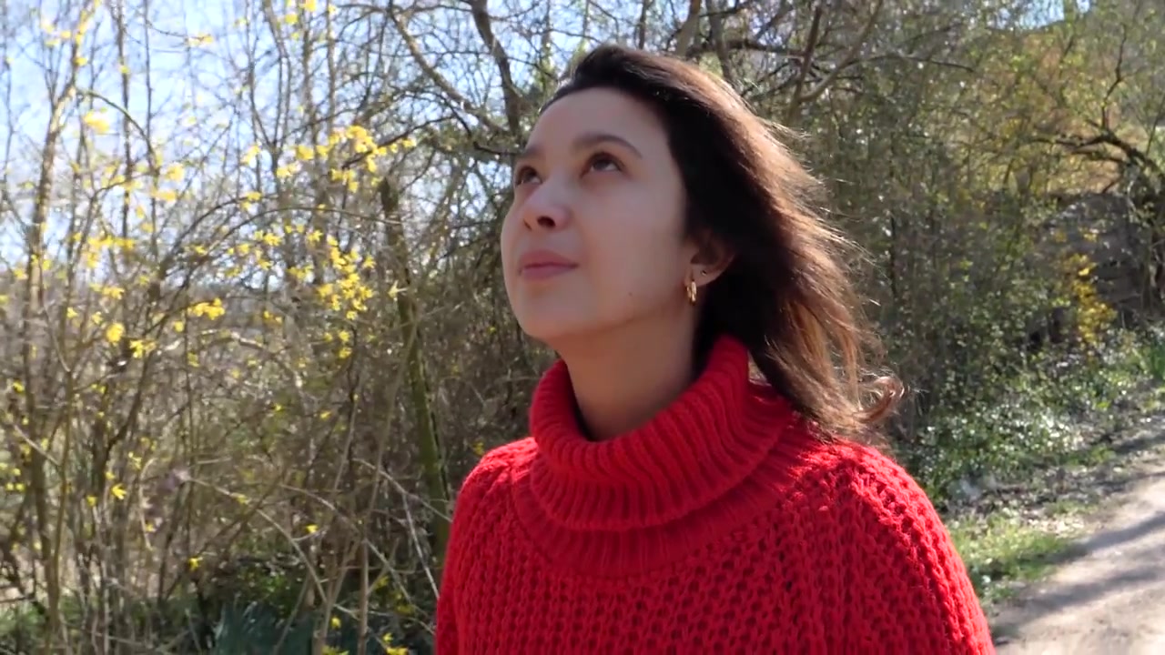 Toma en cámara lenta de una niña con vestido rojo mirando a su alrededor y sonriendo mientras camina por el bosque