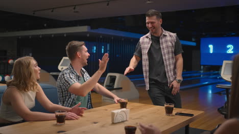 un hombre con una camisa a cuadros en un club de bolos corre felizmente a sus amigos para celebrar la racha de noqueos. comparte la victoria con tus amigos. grupo multiétnico de amigos