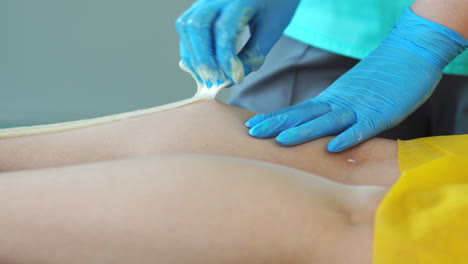 two girls in a beauty salon master in a bathrobe and gloves doing the procedure to remove hair on the legs with a sugar mixture