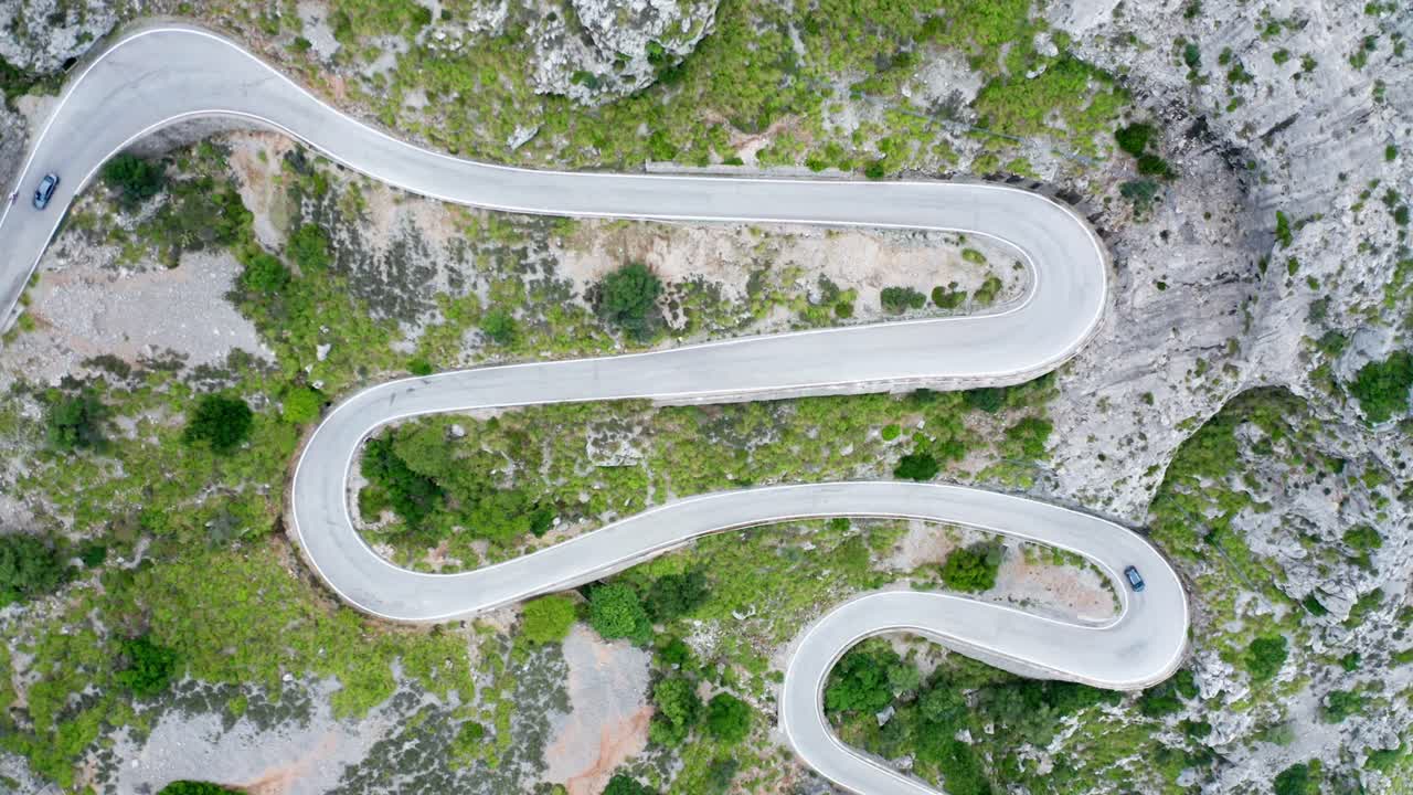 Cars on winding curvy road through green forested stony mountain range, drone aerial view