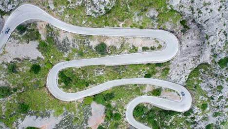 cars on winding curvy road through green forested stony mountain range, drone aerial view