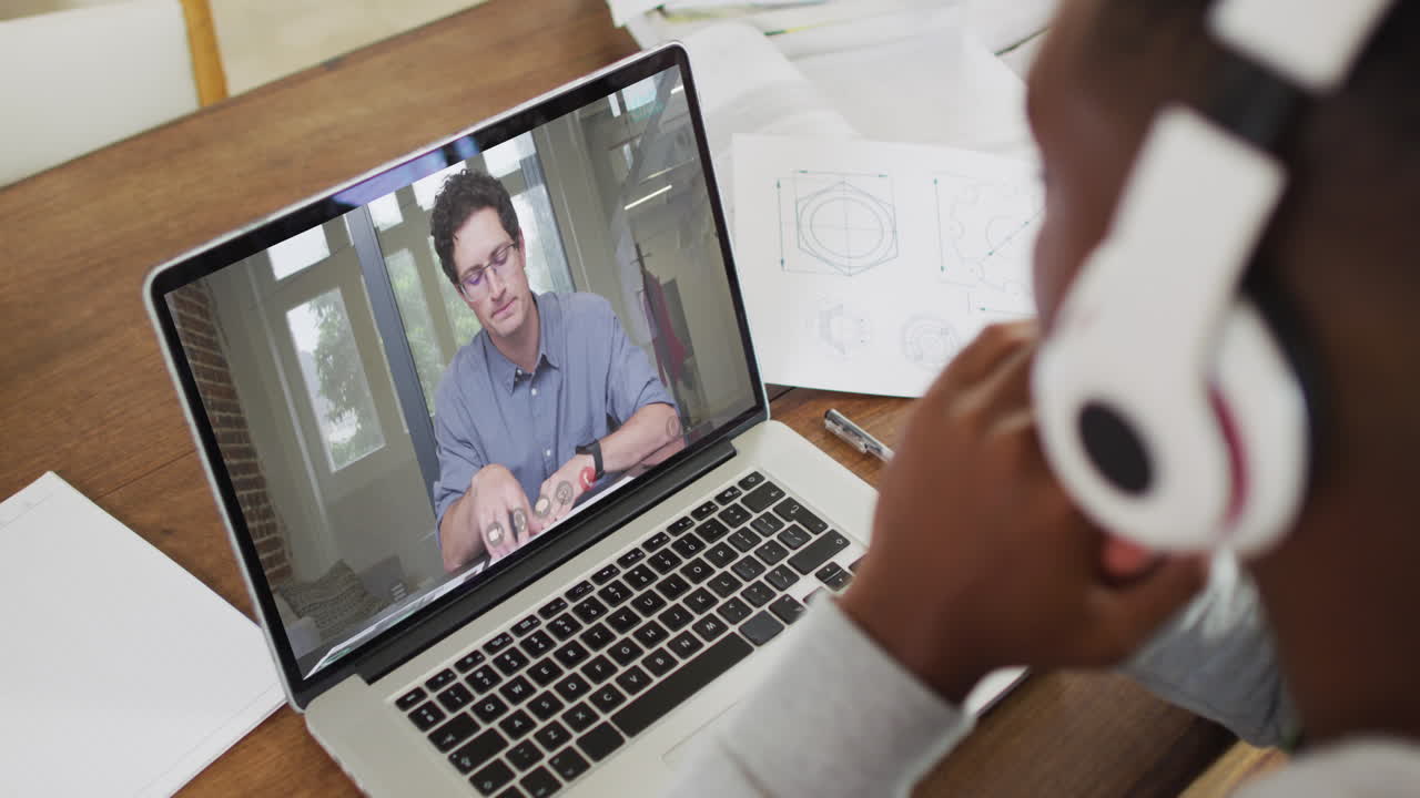 African american male college student wearing headphones having a video call on laptop at home