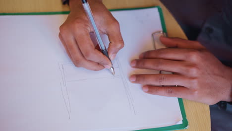 close-up of male hands drawing technical sketch on white sheet using ballpoint pen during creative planning session, focusing on lines and layout structure on clipboard placed on wooden table indoors