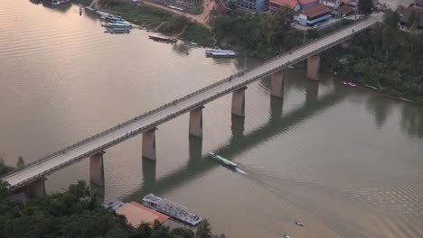 boat-going-under-a-bridge-on-the-river-in-the-mountain-town-of-Nong-Khiaw-in-Laos,-Southeast-Asia