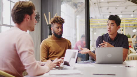 three young male creative colleagues brainstorming in a meeting room, close up