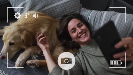 camera interface against caucasian woman talking a selfie with her dog on the couch