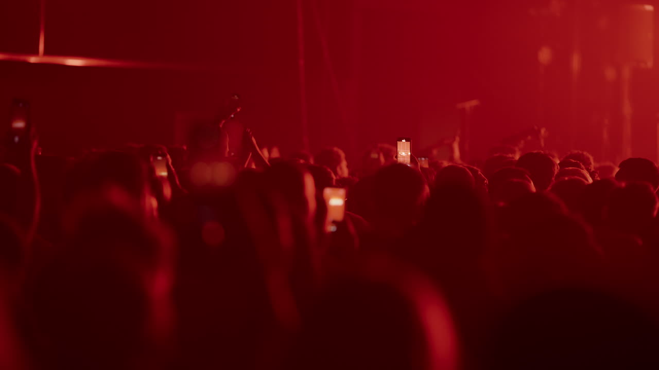 Silhouette di spettatori a un concerto che registrano con i telefoni in luce rossa