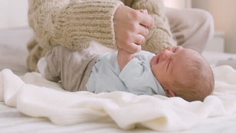 loving young mother calming down and cuddling her crying newborn baby on the bed at home