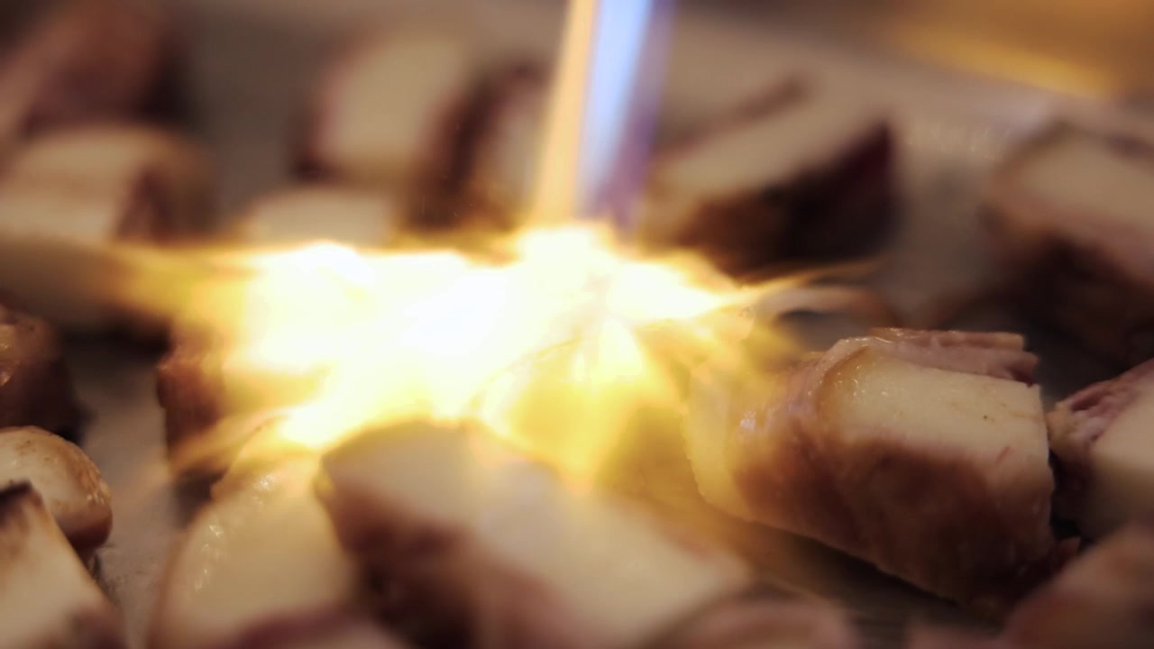 Primo piano di formaggio avvolto nel prosciutto grigliato alla fiamma con un cannello da cucina, per creare un drammatico antipasto gourmet durante la preparazione professionale del cibo