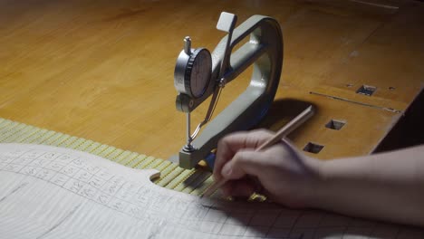 Stringed instrument maker master luthier proceed with graduation work in cello back plate, use thickness gauge caliper, measure levels, use pencil write values on wood , Cremona, Italy workshop