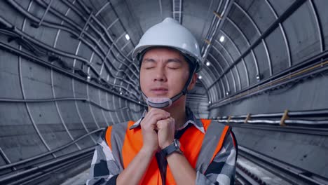 Close Up Of Asian Male Engineer With Safety Helmet Pray For Something While Standing In Underground Subway Tunnel