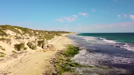 a serene beach coastline with waves, green vegetation, and sandy cliffs, aerial view