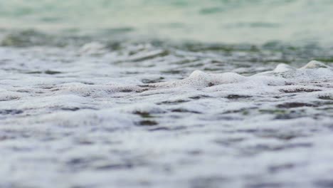 flowing sea water on the beach with white foam in the evening. the edge of the ocean with foam waves hitting into the shoreline background. close-up.