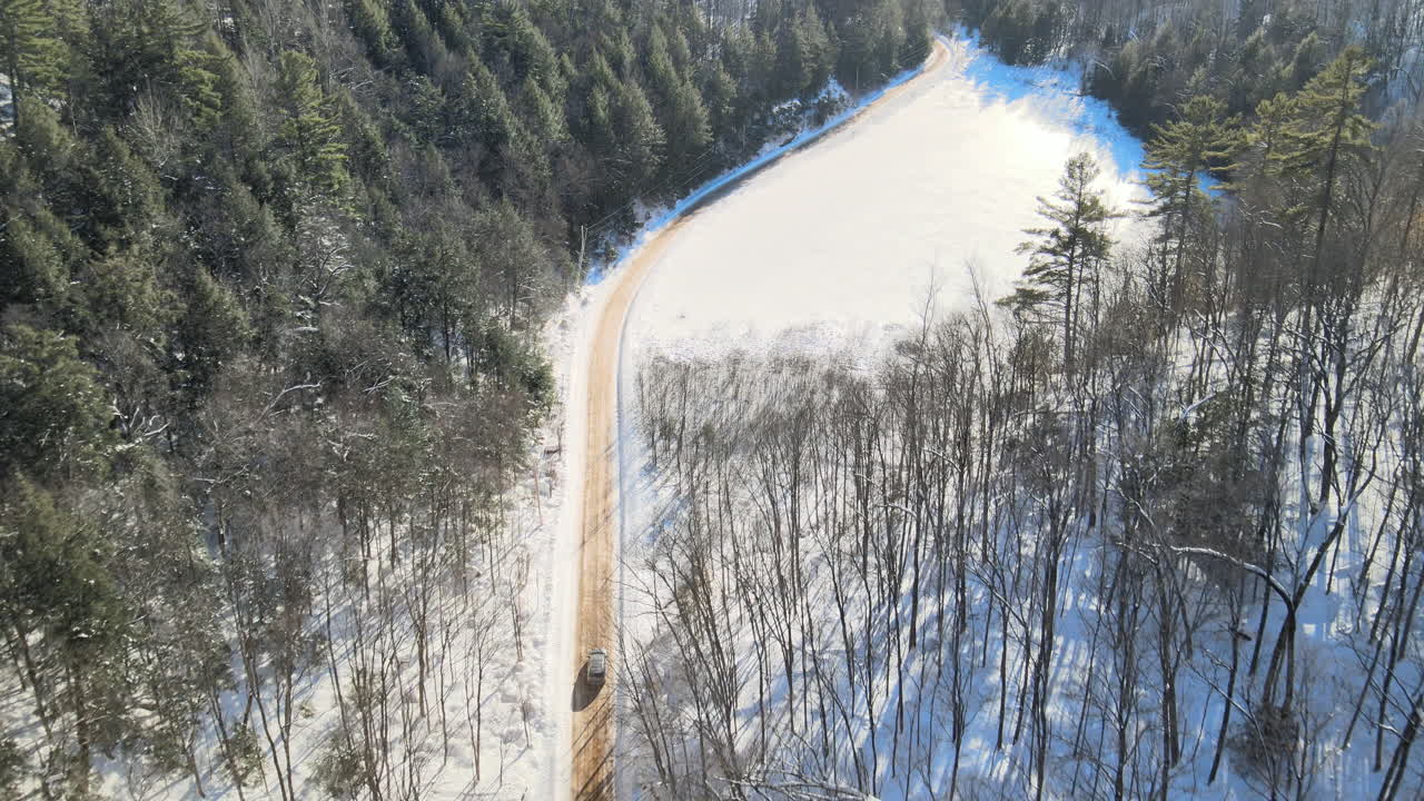un vehículo conduce a lo largo de una carretera de invierno en el campo, visto desde un dron por encima