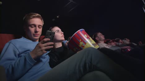 young man using smartphone in movie theatre. young man using phone in cinema