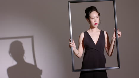 spotlight casting shadow guiding asian woman sliding large frame diagonally in studio, copy space