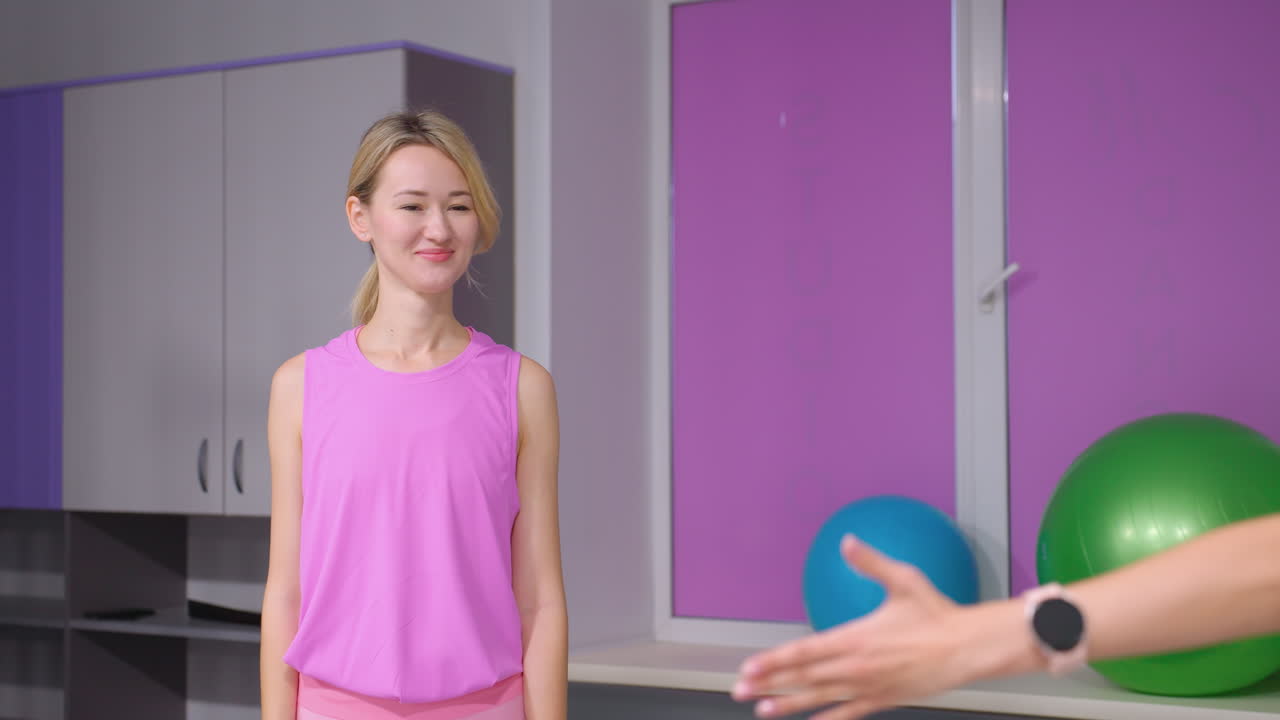 joven dama en olas rosas en amigo con sonrisa cálida en gimnasio elegante con decoración pastel, casilleros, equipos de fitness, pelota de ejercicio, y atmósfera acogedora, y interacción amistosa