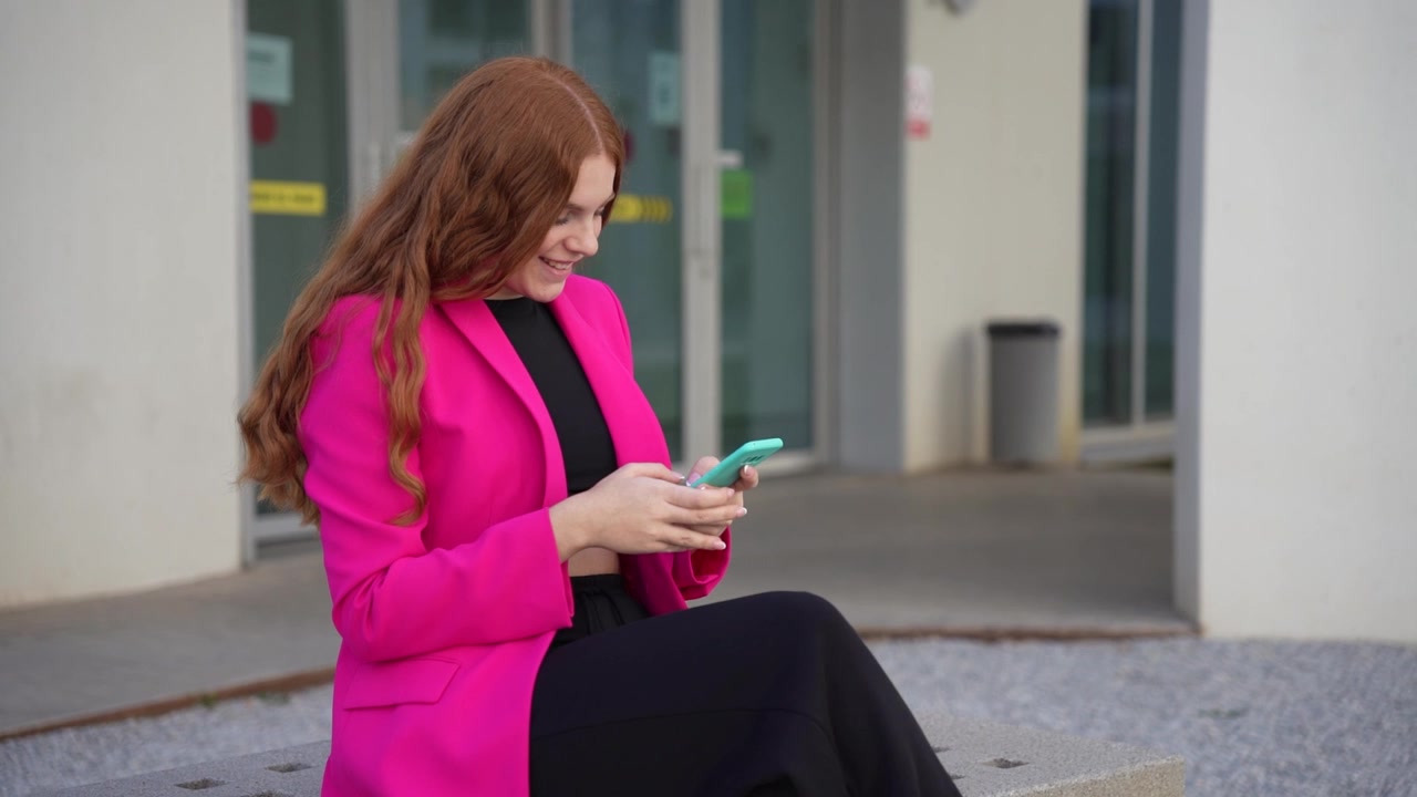 Eine selbstbewusste Geschäftsfrau in einem leuchtend pinken Blazer beschäftigt sich mit ihrem Smartphone.