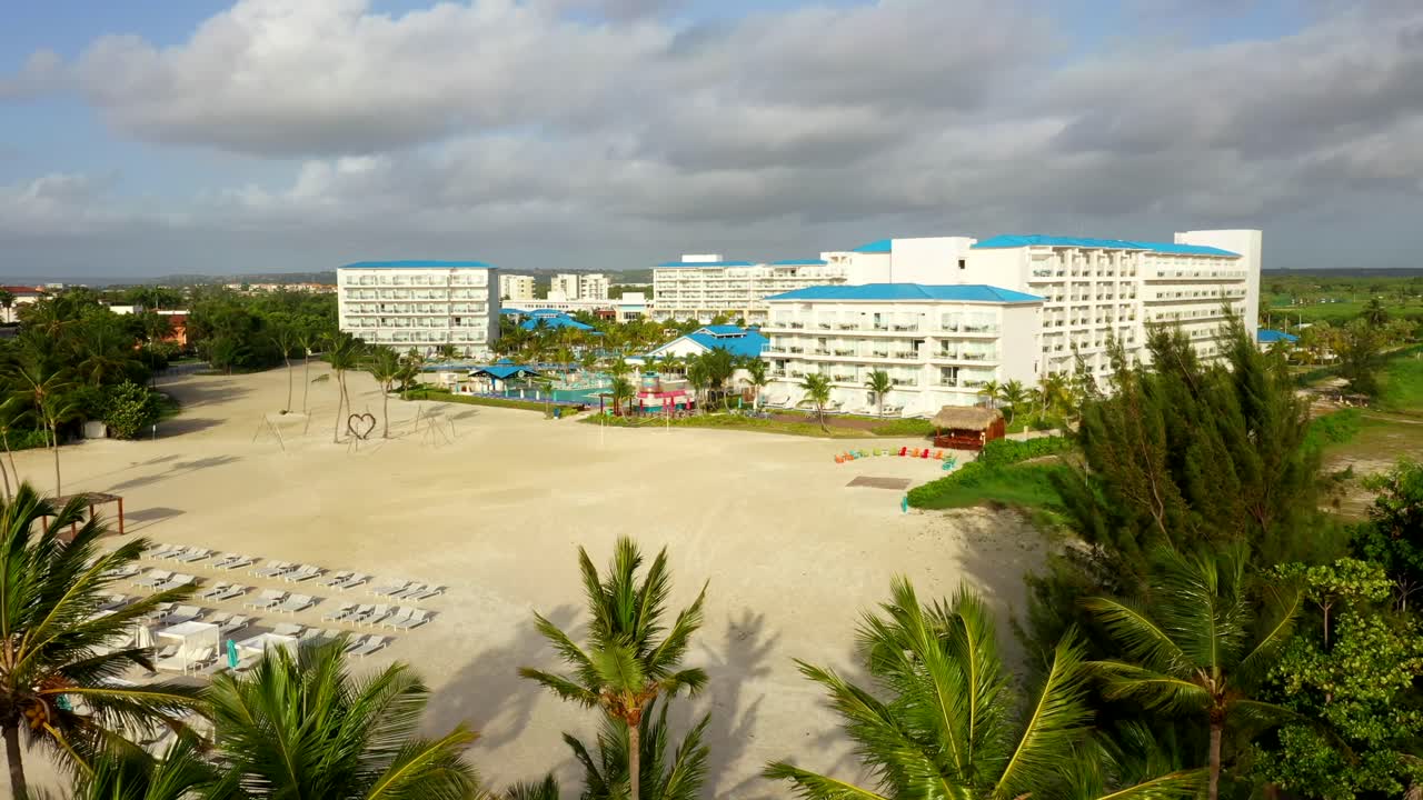 Resort entrance aerial surrounded by palm trees under blue sky, aerial approach, Cap Cana Juanillo Beach Dominican Republic