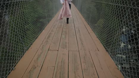 mujer viajera con chaqueta rosa en la pasarela colgante sobre el río coaticook en los municipios del este, quebec, canadá, cámara lenta