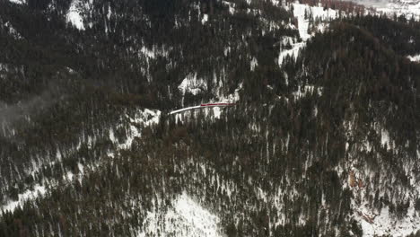 Tiro-Aéreo-Alto-Sobre-El-Bosque-Con-Un-Viaducto-En-El-Centro-Mientras-Pasa-Un-Tren-Rojo