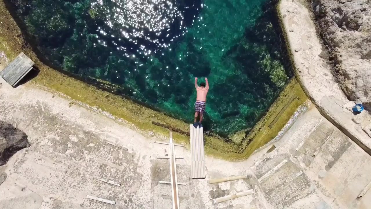 Uomo che si tuffa nell'acqua cristallina da un pontile di legno a Cala s'Estaca Valldemossa Mallorca