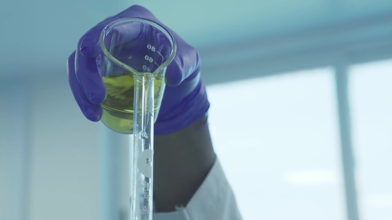A scientist is pouring yellow coloured chemical from a beaker to test tube.