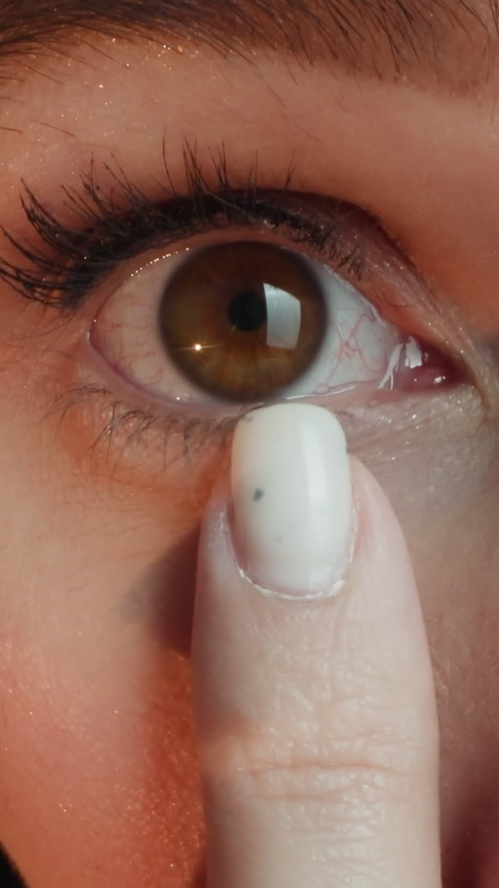 Young woman blends concealer under eye with finger to cover flaws. Brunette lady applies cosmetic product on soft skin before doing makeup macro