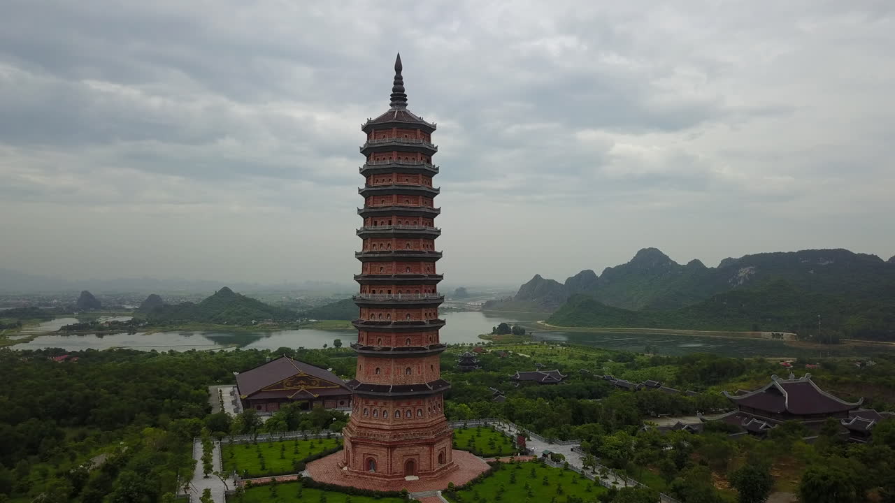 This detailed shot showcases the impressive architecture of Bái Đính Pagoda in Ninh Binh, Vietnam, with the surrounding serene landscape and karst mountains in the background under a cloudy sky