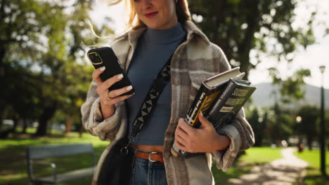 woman holding phone and books outdoors