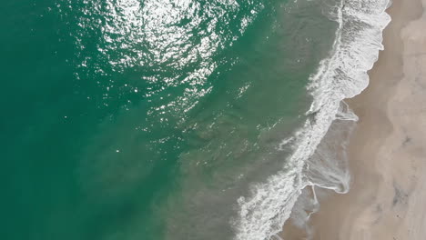 Toma-Aérea-De-Arriba-Hacia-Abajo-Volando-A-Lo-Largo-De-Una-Playa-Con-Las-Olas-Rodando-Durante-La-Tarde