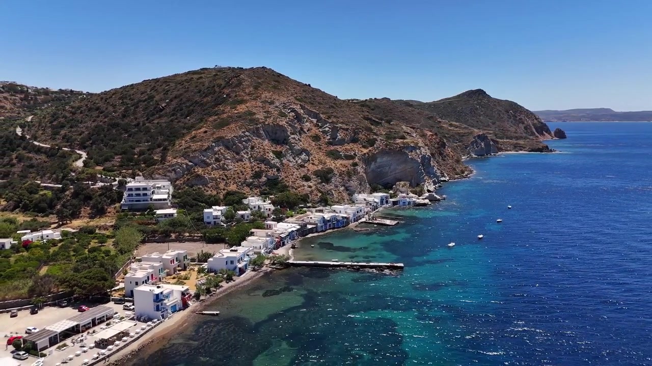 Vissersdorp Klima en kleurrijke syrmata boothuizen strekken zich uit langs een ruige vulkanische kustlijn naast helder Egeïsch water, Milos, Griekenland, drone-uitzoomen
