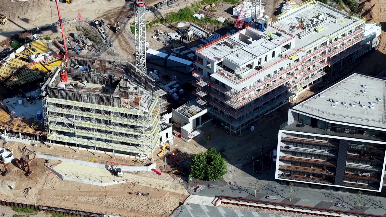 Video dinámico de dron captura una vista cenital de una obra en construcción activa con grúas, edificios modernos tomando forma, hormigón, acero y la vibrante luz solar matutina
