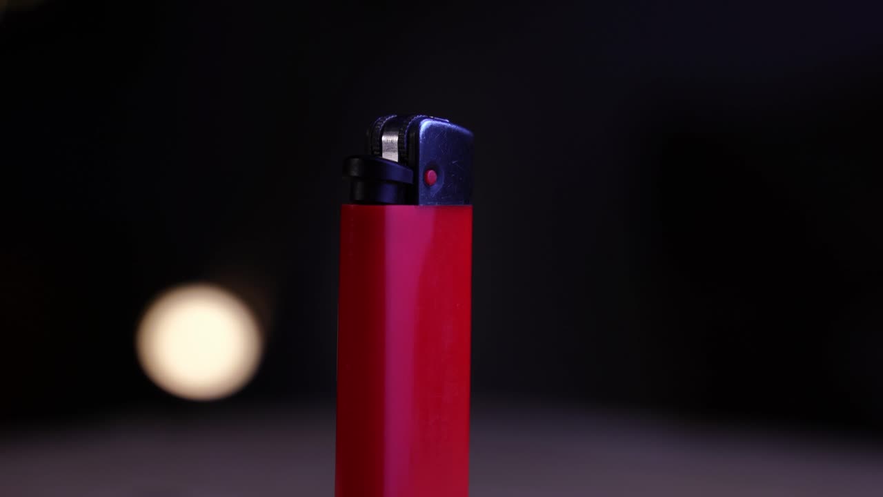Black tip of a red lighter behind dark background with small light in background