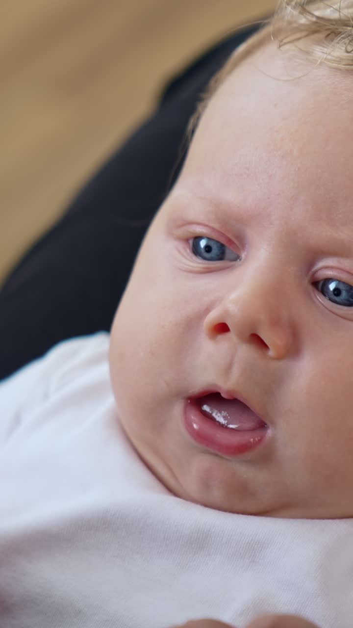 Lovely Caucasian fair-haired child with big blue eyes. Close up portrait. Baby showing tongue to parent. Vertical video