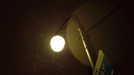 dimly lit streetlamp surrounded by light snowfall on a quiet night in downtown st. catharines, low angle looking up to glowing warm light