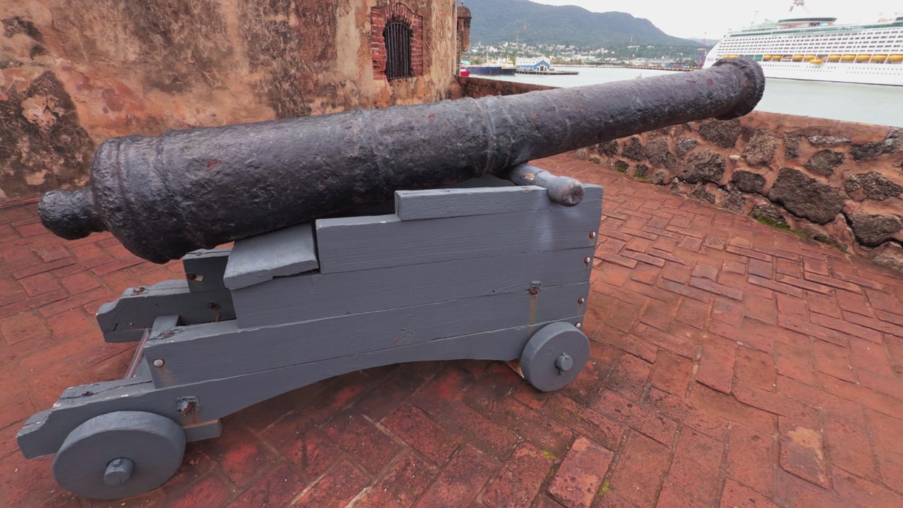 Antique cannon at historic Fortaleza San Felipe overlooking the port with a modern cruise ship in background in Puerto Plata, Dominican Republic
