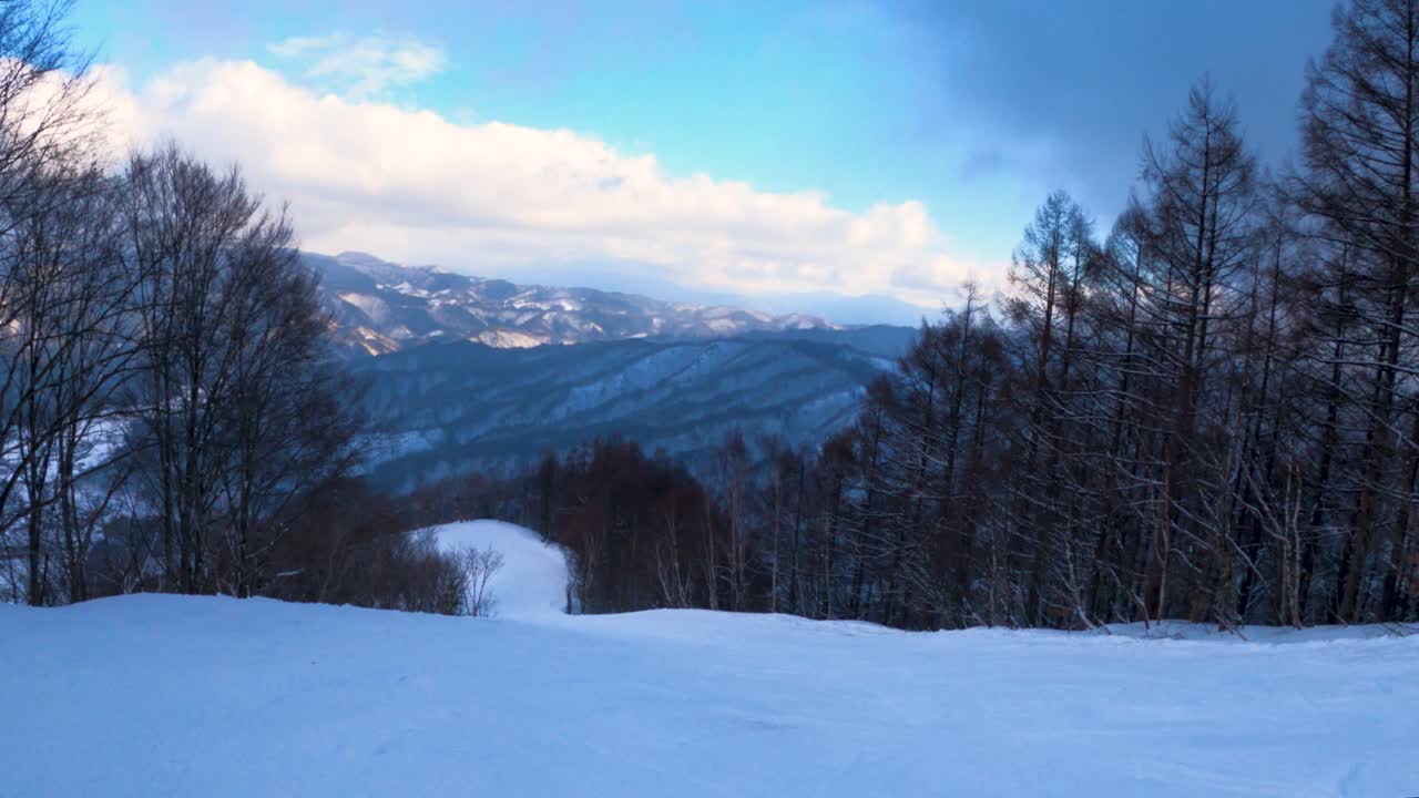 Descendo uma pista de esqui, vista em primeira pessoa com as Montanhas Hida ao fundo, Japão.