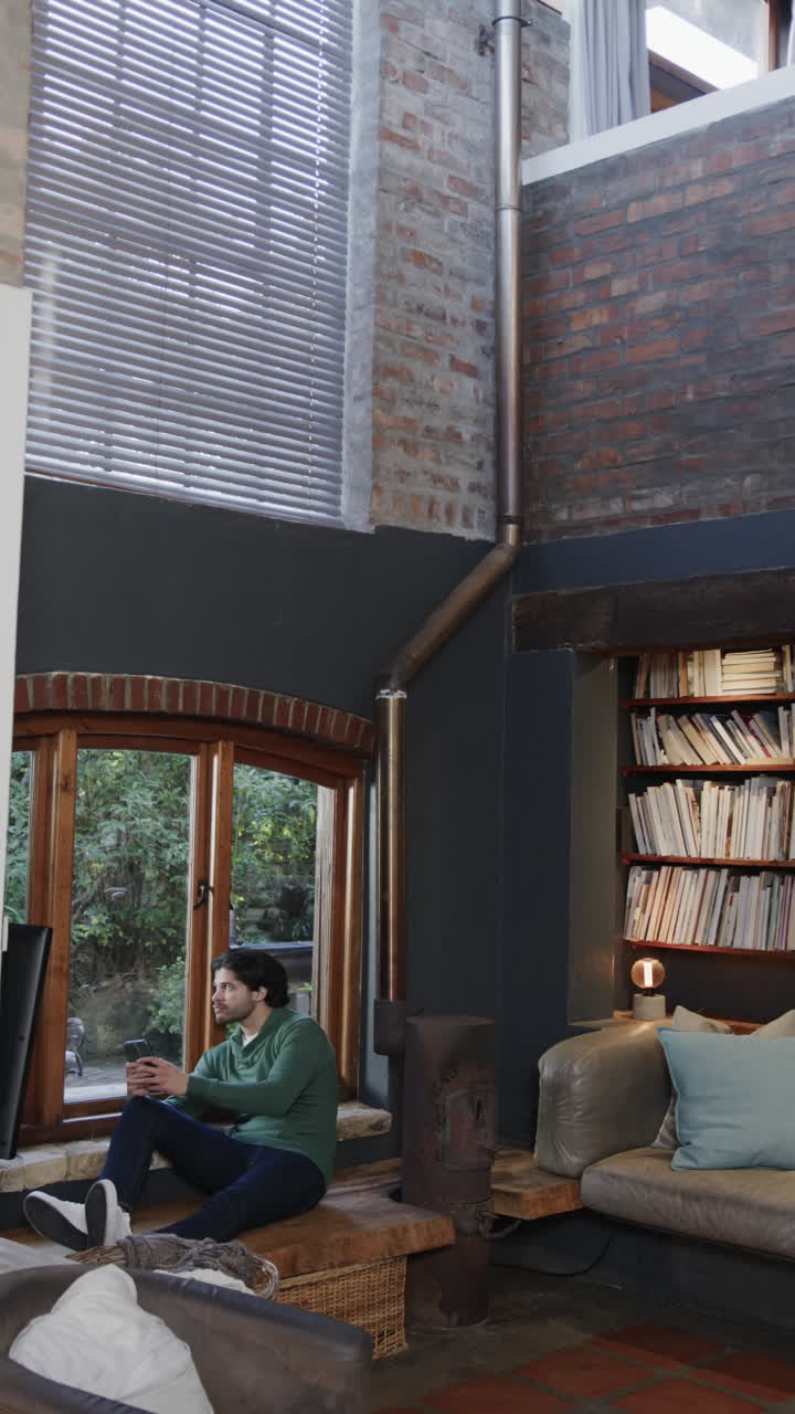 Vertical video of biracial man using smartphone in living room, slow motion