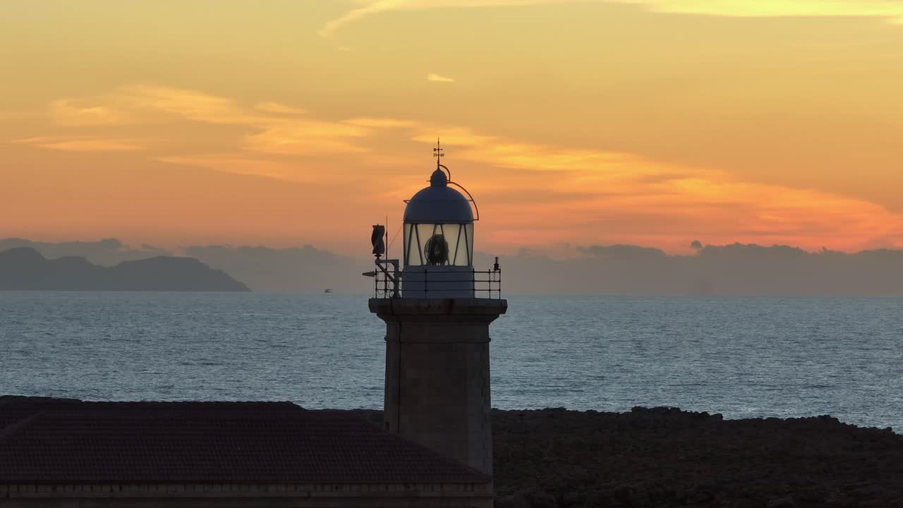 órbita de zoom largo aéreo alrededor del faro de punta nati durante la puesta de sol de la hora dorada en menorca, españa
