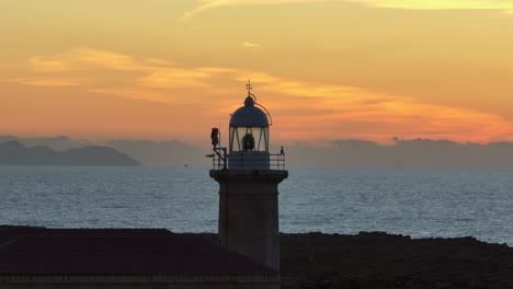 aerial long zoom orbit around punta nati lighthouse during golden hour sunset in menorca, spain