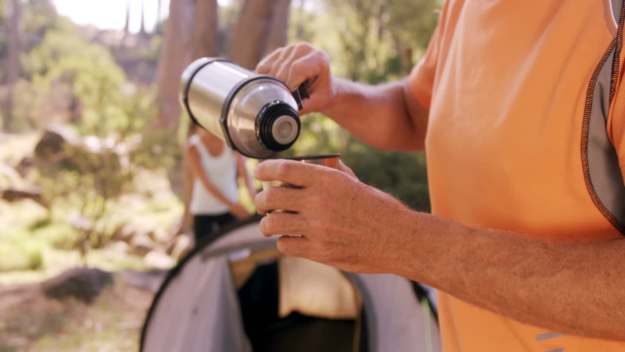 hombre vertiendo el agua potable en taza en el campamento