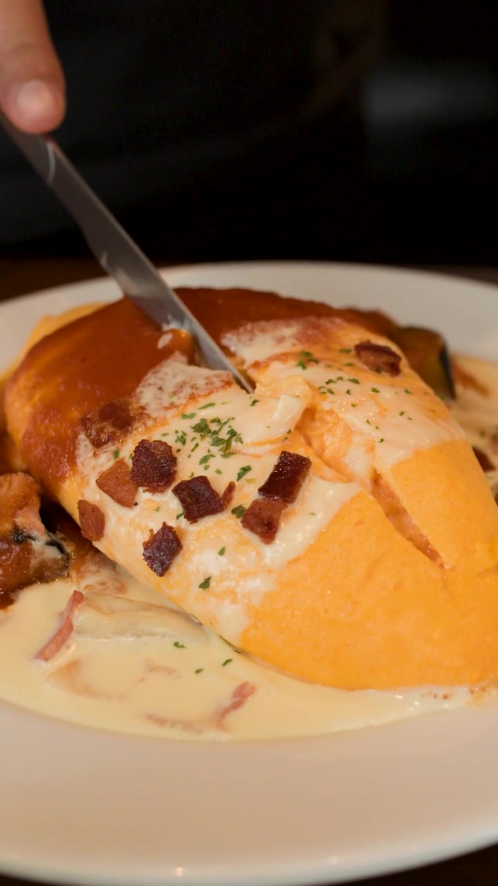 Una mano usa un coltello per tagliare un omurice soffice condito con salsa cremosa