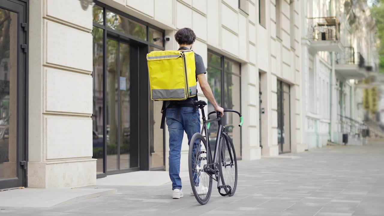 hombre de entrega caminando con bicicleta y bolsa amarilla, vista trasera