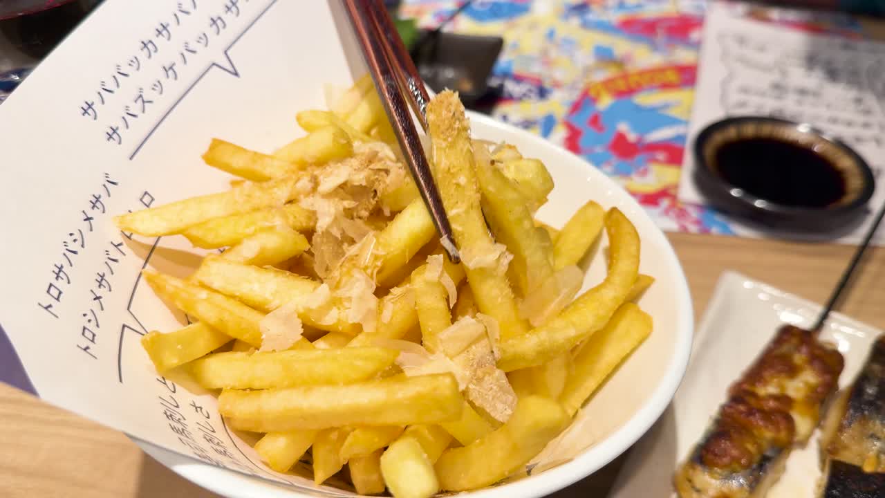 Close-up shot of chopsticks picking up crispy french fries topped with dancing bonito flakes