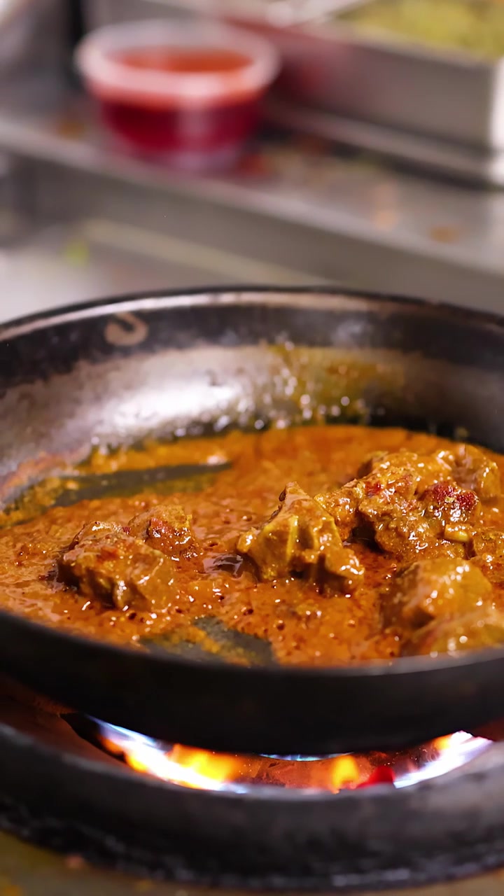 Primo piano di curry di carne piccante che sobbolle in una padella su una fiamma a gas aperta