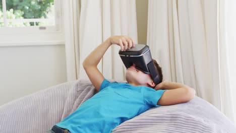 niño caucásico usando auriculares vr mientras está acostado en la bolsa de frijoles en casa