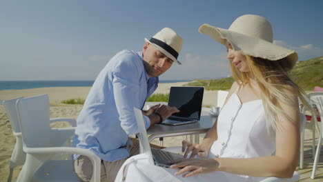 pareja hablando y usando computadoras portátiles en la playa