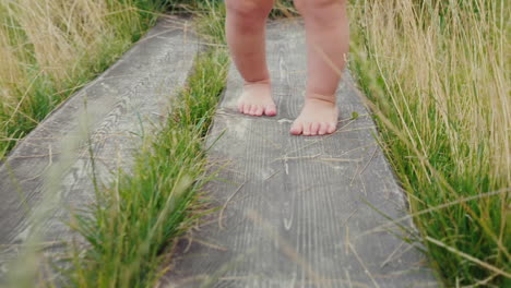 the legs of the baby make the first unsteady steps along the wooden path among the grass first succe